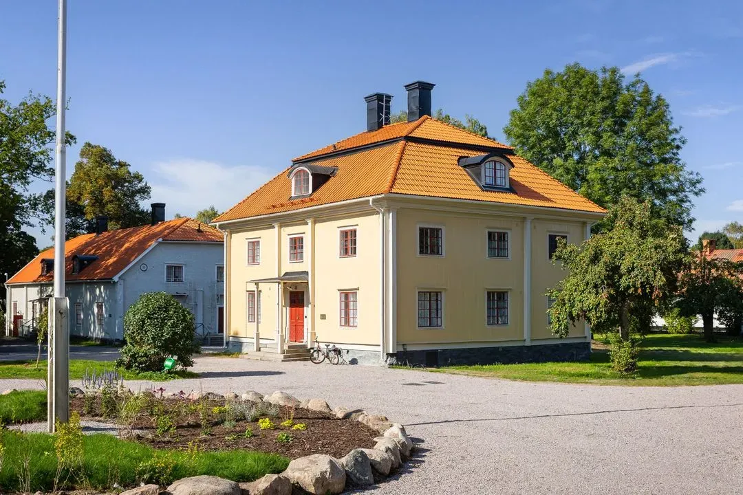 Brukshusets gula fasad och entré omgivna av planteringar.