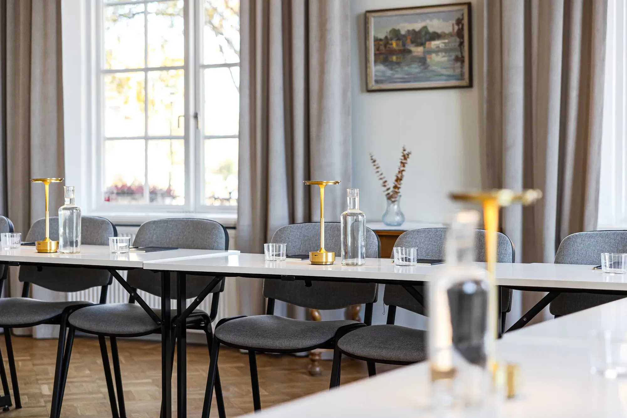 Ljust konferensrum med dukade bord, vattenkaraffer och mässingslampor.