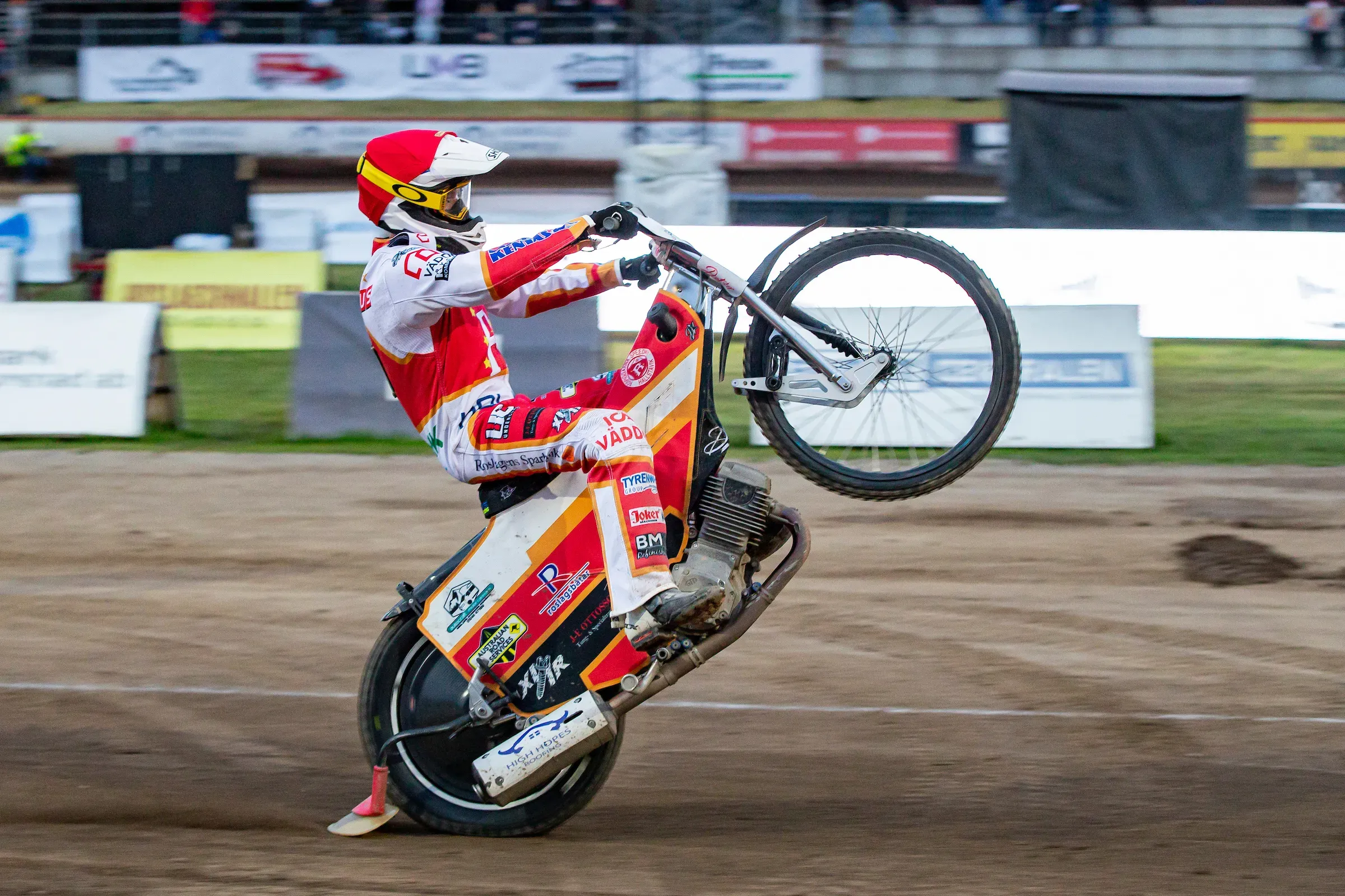 Speedwayförare gör en wheelie under en tävling.