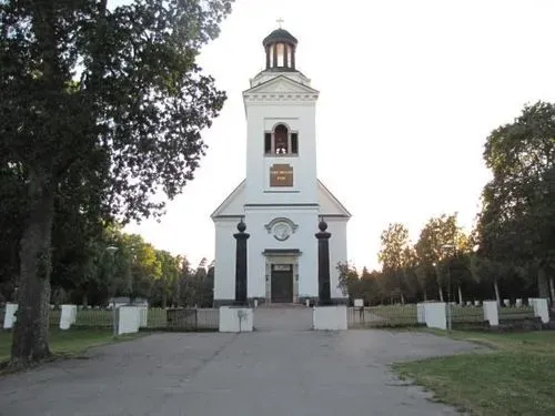 Söderfors kyrkas ljusa fasad och torn omgivet av grönska.