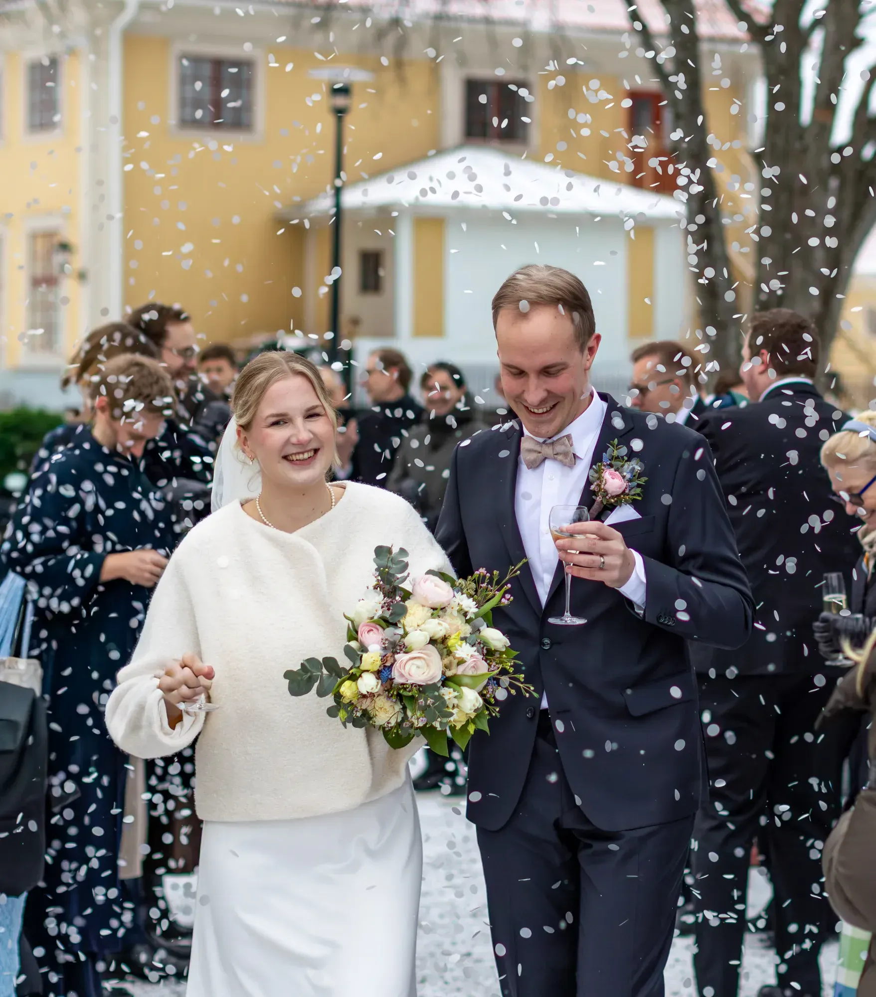 Brudpar och gäster firar med konfetti framför herrgården.